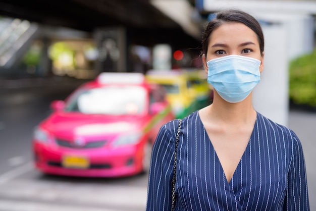 Giovane imprenditrice asiatica con maschera alla stazione dei taxi per le strade della città