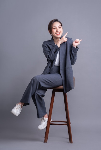 Giovane imprenditrice asiatica seduta su una sedia e in posa su sfondo grigio