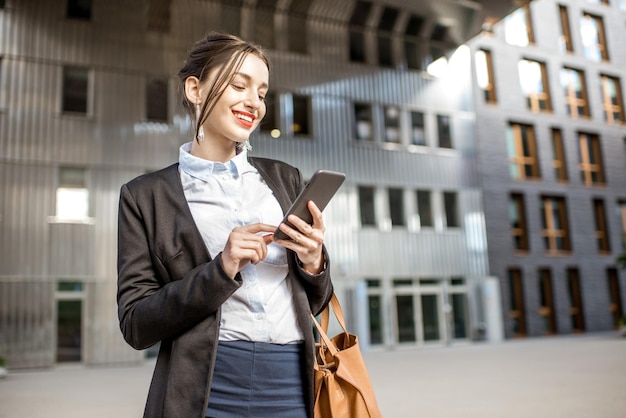 Giovane imprenditrice che utilizza il telefono all'aperto nel moderno quartiere degli uffici