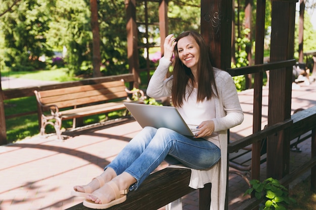 Giovane imprenditrice di successo in abiti casual leggeri. Donna sorridente che lavora al computer pc portatile moderno nel parco cittadino in strada all'aperto sulla natura primaverile. Ufficio Mobile. Concetto di business freelance.