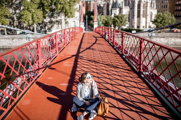 Giovane imprenditrice elegante seduta con telefono e borsa sulla passerella rossa a Lione, Francia