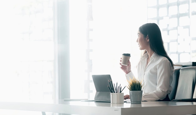 Giovane imprenditrice esecutiva tenendo la tazza di caffè e rilassarsi mentre era seduto alla sua scrivania durante il lavoro.