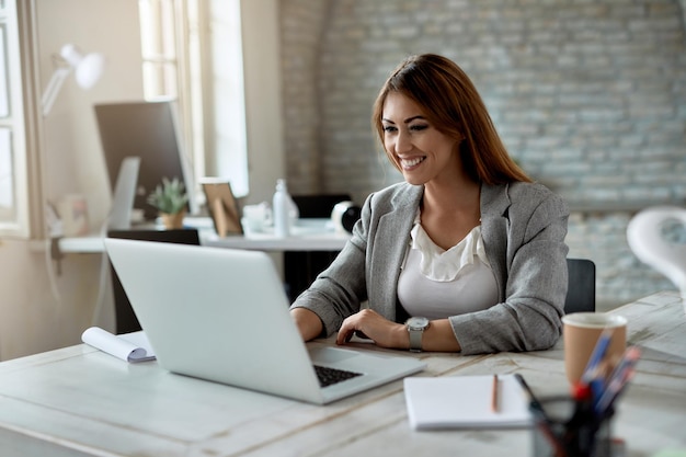 Giovane imprenditrice felice utilizzando il computer mentre si lavora in ufficio