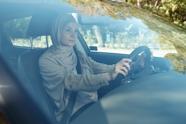 Giovane imprenditrice in hijab tenendo per il volante mentre si guida l'auto