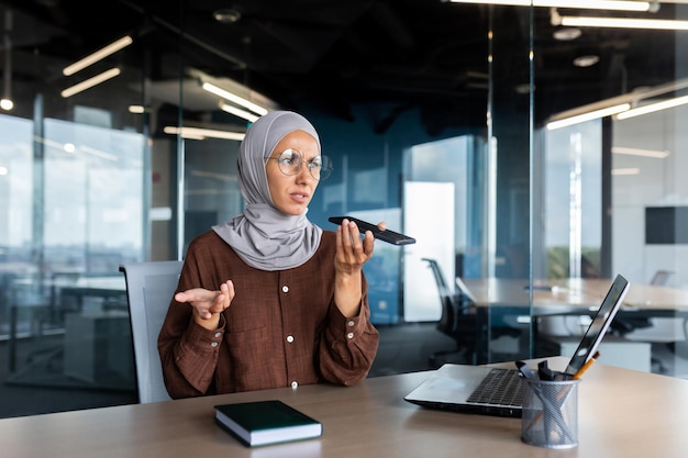 Giovane imprenditrice musulmana preoccupata in hijab seduta in ufficio e che parla al telefono