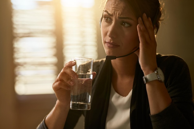 Giovane imprenditrice sconvolta che beve un bicchiere d'acqua mentre lavora in ufficio