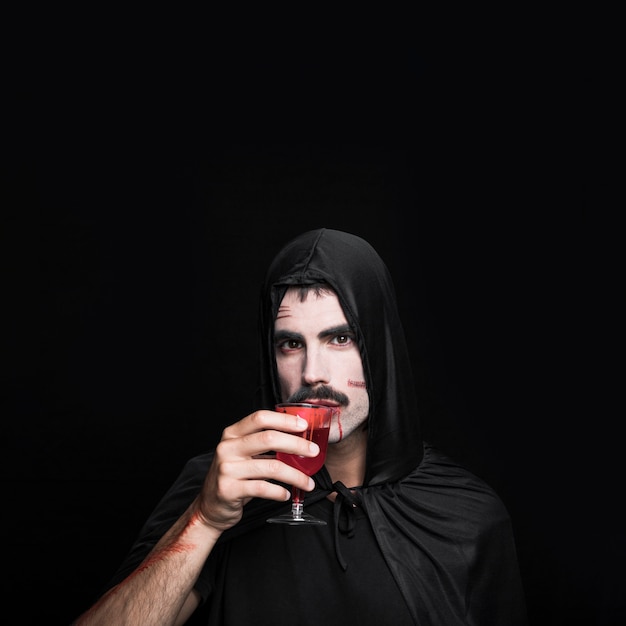 Giovane in costume di Halloween che beve liquido rosso in studio