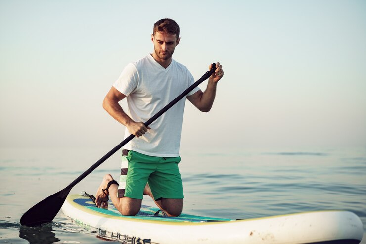 Foto giovane in maglietta e pantaloncini che galleggia sulla tavola da sup