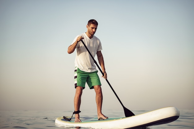 Giovane in maglietta e pantaloncini che galleggia sulla tavola da sup