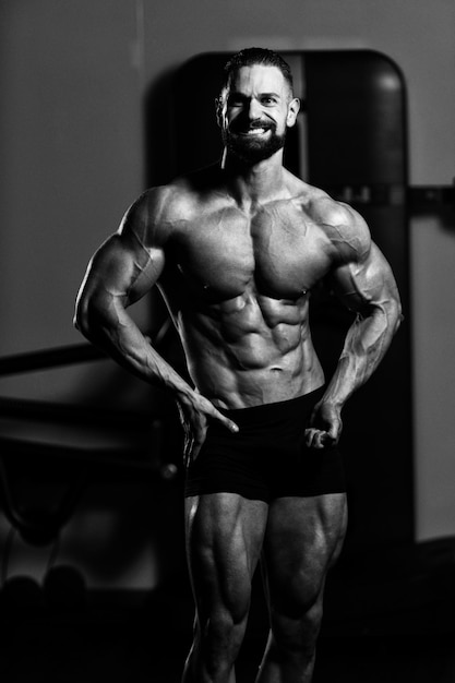 Giovane in piedi forte in palestra e flettendo i muscoli muscoloso atletico bodybuilder modello di fitness in posa dopo gli esercizi