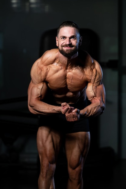 Giovane in piedi forte in palestra e flettendo i muscoli muscoloso atletico bodybuilder modello di fitness in posa dopo gli esercizi