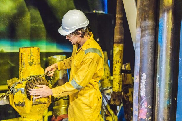 Giovane in un'uniforme da lavoro gialla occhiali e casco in ambiente industriale piattaforma petrolifera o