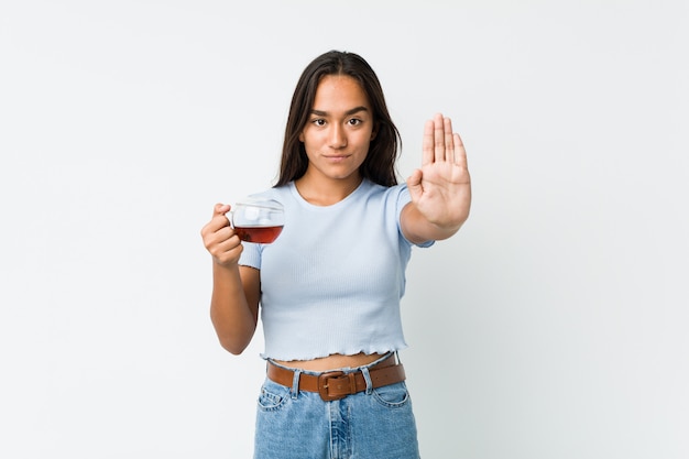 Giovane indiano che tiene una tazza di tè che sta con il fanale di arresto di rappresentazione della mano tesa