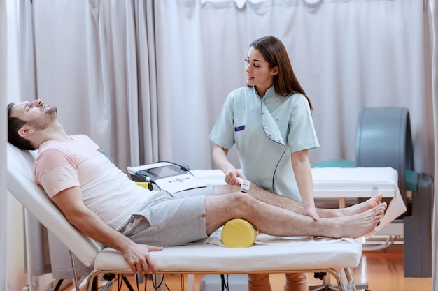 Giovane infermiera femminile caucasica che per mezzo del dispositivo di elettrolisi per guarire le lesioni al ginocchio dei pazienti.