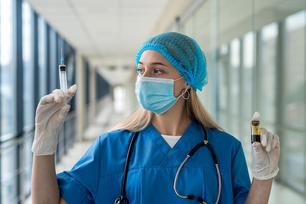 Giovane infermiera in uniforme e maschera che tiene una siringa nelle sue mani sul corridoio