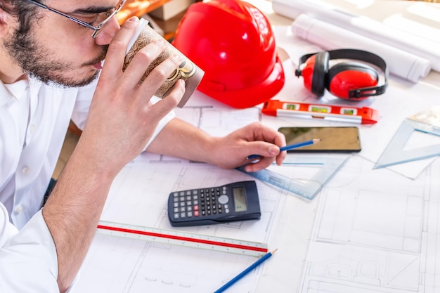 Giovane ingegnere architetto che beve caffè mentre lavora ai piani