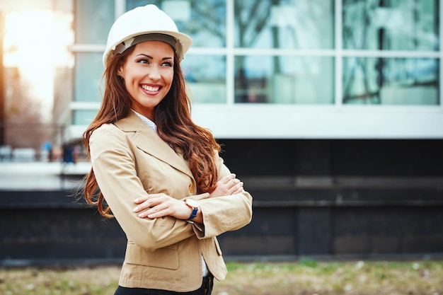 Giovane ingegnere femminile di successo con casco bianco in piedi sullo sfondo della città urbana.