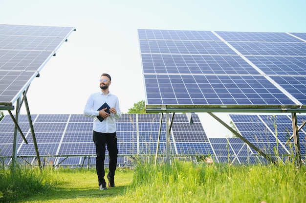 Giovane ingegnere in camicia bianca che tiene un tablet e verifica i pannelli fotovoltaici presso la centrale solare Copia lo spazio per il tuo testo