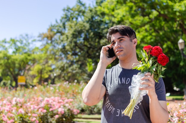 Giovane innamorato dei fiori in mano nel parco che parla al telefono con la sua ragazza