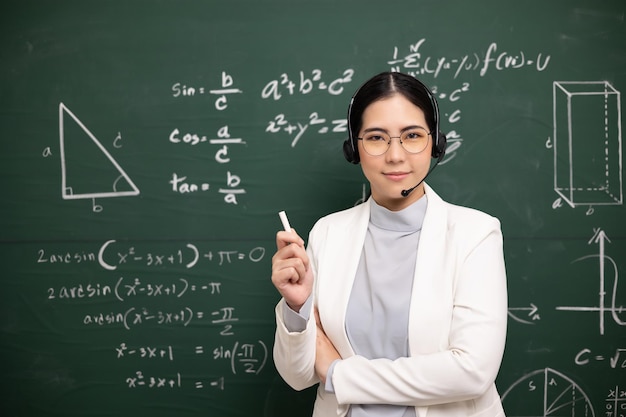 Giovane insegnante asiatica che tiene il gesso per insegnare la videoconferenza con lo studente Insegnante femminile che addestra la matematica nel corso online di lavagna in classe