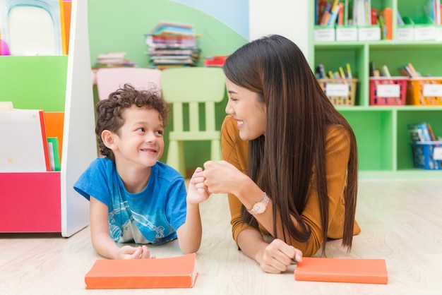 Giovane insegnante asiatico della donna che insegna al bambino americano nell&#39;aula di asilo con felicità e rilassamento. Istruzione, scuola elementare, apprendimento e concetto della gente - l&#39;insegnante aiuta l&#39;aula dei bambini della scuola.