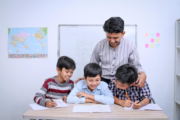 Giovane insegnante asiatico e felici studenti multietnici elementari che leggono un libro insieme in classe