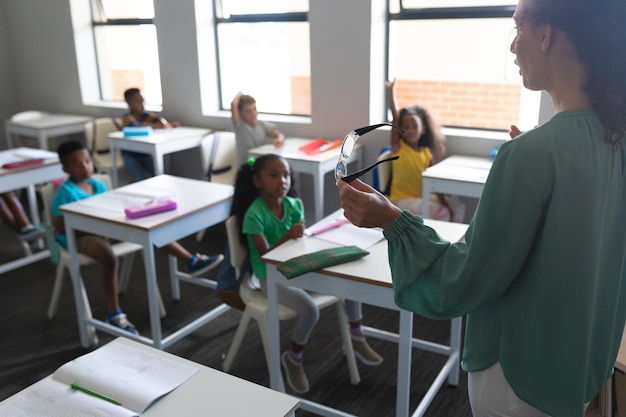 Giovane insegnante caucasica che insegna a studenti di scuola elementare multirazziale seduti alla scrivania