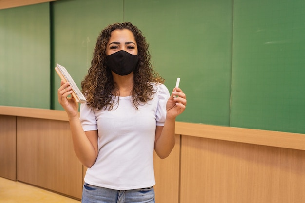 Giovane insegnante con gesso e gomma in mano che indossa una maschera chirurgica nella nuova normalità.