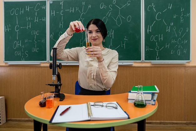 Giovane insegnante con microscopio, libro e provette in un'aula. lezione di chimica