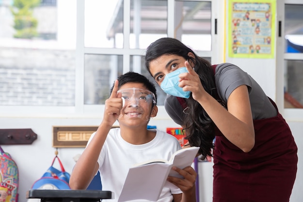 Giovane insegnante messicana e bambino in classe, con maschera facciale, concetto di educazione prescolare