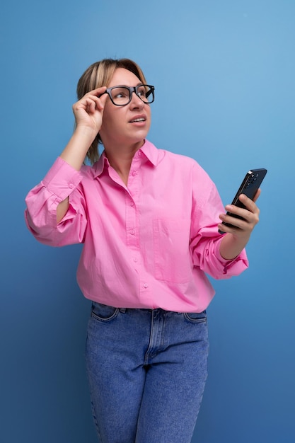 Giovane intelligente elegante donna d'affari bionda con gli occhiali vestita con una camicia rosa risolve problemi di lavoro sul