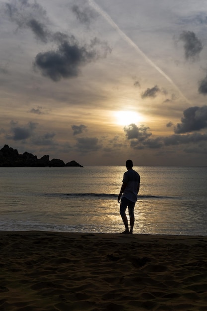 Giovane irriconoscibile che guarda il tramonto sulla riva della spiaggia