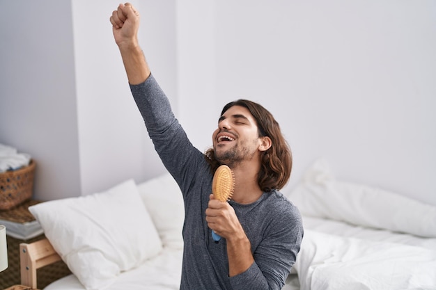 Giovane ispanico che canta una canzone usando la spazzola come microfono in camera da letto