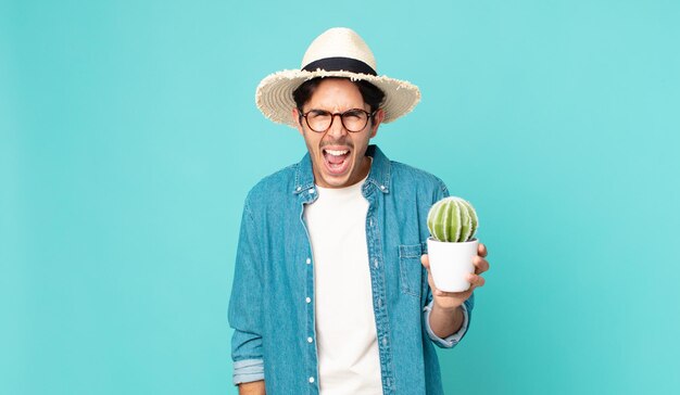 Giovane ispanico che grida in modo aggressivo, sembra molto arrabbiato e tiene in mano un cactus