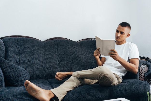 Giovane ispanico che legge un libro, uomo che studia, seduto sul divano.