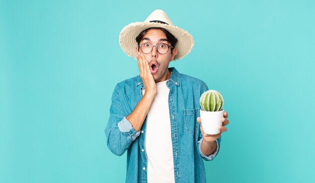 Giovane ispanico che si sente scioccato e spaventato e tiene in mano un cactus