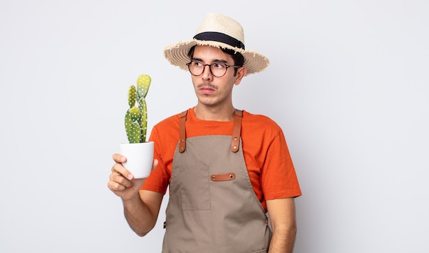 giovane ispanico che si sente triste, turbato o arrabbiato e guarda di lato. giardiniere con concetto di cactus