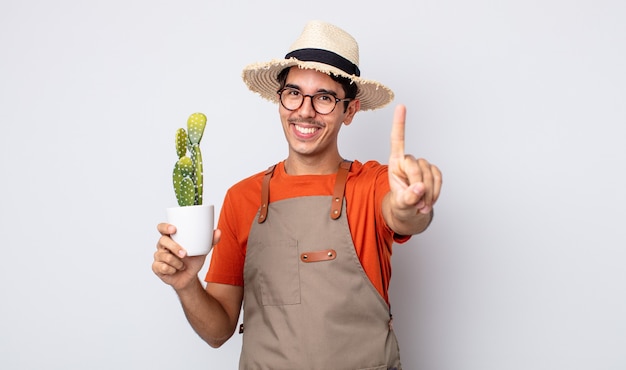 Giovane ispanico che sorride con orgoglio e sicurezza facendo il numero uno. giardiniere con concetto di cactus