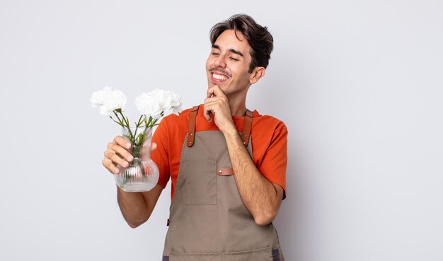 Giovane ispanico che sorride con un'espressione felice e sicura con la mano sul mento. concetto di fiorista