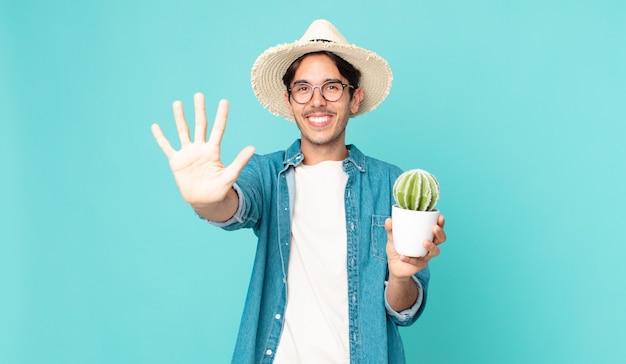 Giovane ispanico che sorride e sembra amichevole, mostra il numero cinque e tiene in mano un cactus