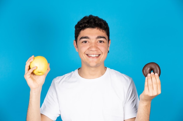 Giovane ispanico che tiene una ciambella di frutta e cioccolato o ciambella sulle mani e guardando la fotocamera