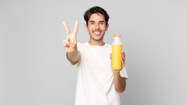 Giovane ispanico sorridente e dall'aspetto amichevole, mostrando il numero due con un thermos di caffè