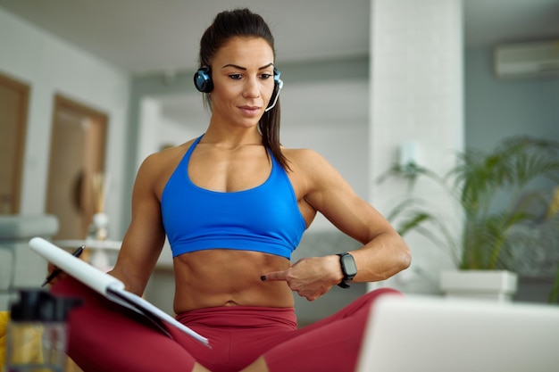 Giovane istruttore di fitness che utilizza il laptop mentre tiene lezione di esercizio online e consiglia i suoi clienti da casa