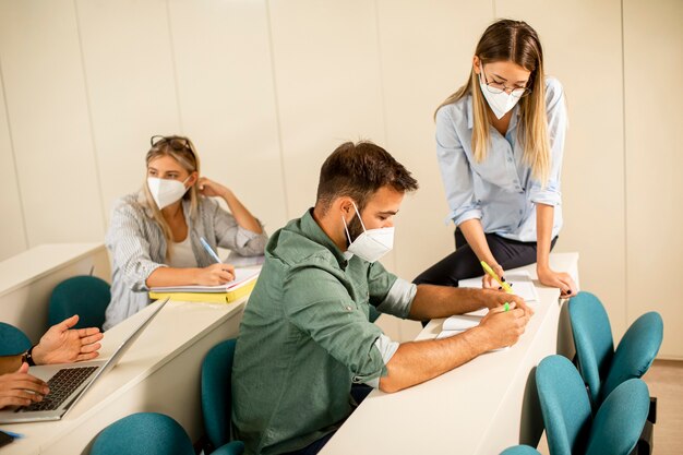 Giovane istruttore femminile che indossa maschera medica protettiva per il viso per la protezione dai virus e aiuta lo studente maschio in aula