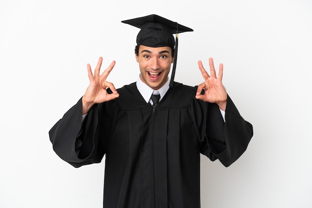 Giovane laureato su sfondo bianco isolato che mostra un segno ok con le dita