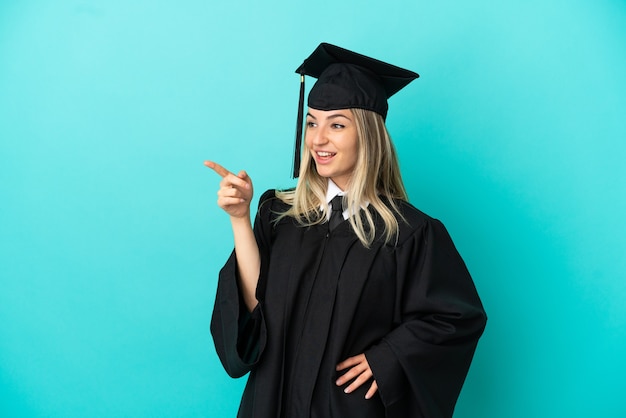Giovane laureato su sfondo blu isolato che punta il dito a lato e presenta un prodotto