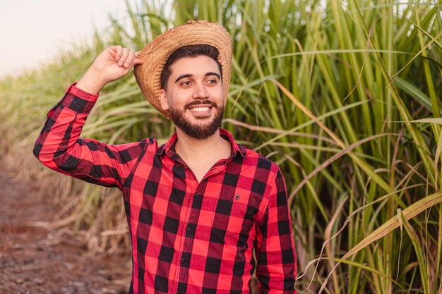 Giovane lavoratore agricolo con cappello di paglia che guarda l'orizzonte con la piantagione di canna da zucchero sullo sfondo