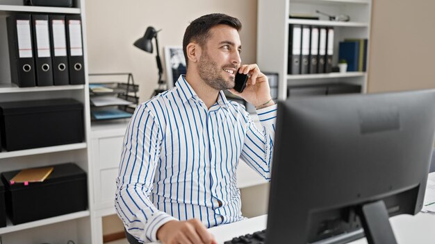 Giovane lavoratore d'affari ispanico che usa il computer e parla sullo smartphone in ufficio