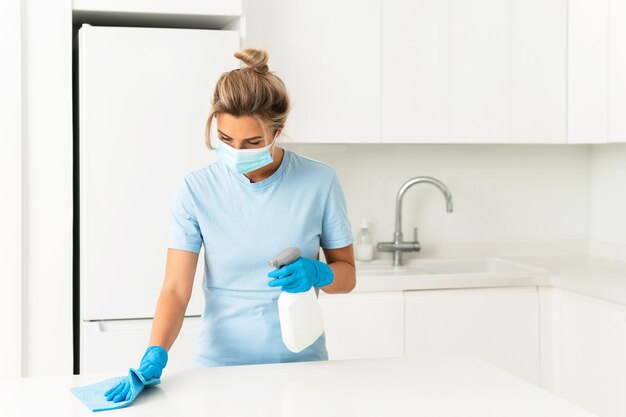 Giovane lavoratrice che indossa maschera e guanti di prevenzione durante la pulizia dell'appartamento