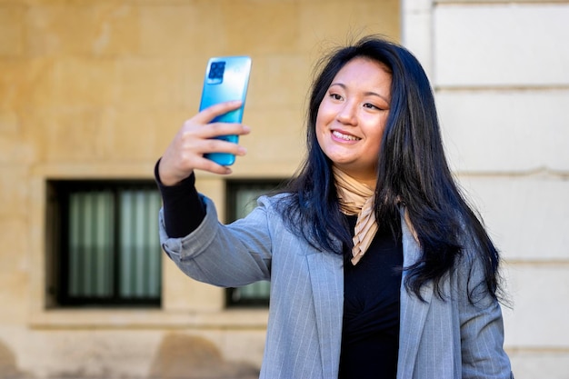 Giovane leader sorridente elegante donna d'affari asiatico occupato che indossa tuta in piedi nella grande città utilizzando il telefono